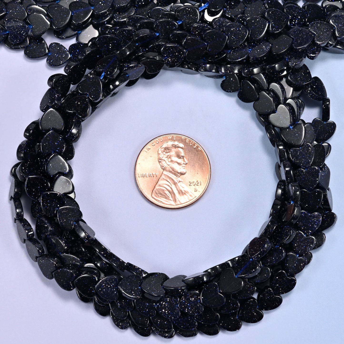 Blue Sandstone flat heart bead strands coiled around a US penny for size reference