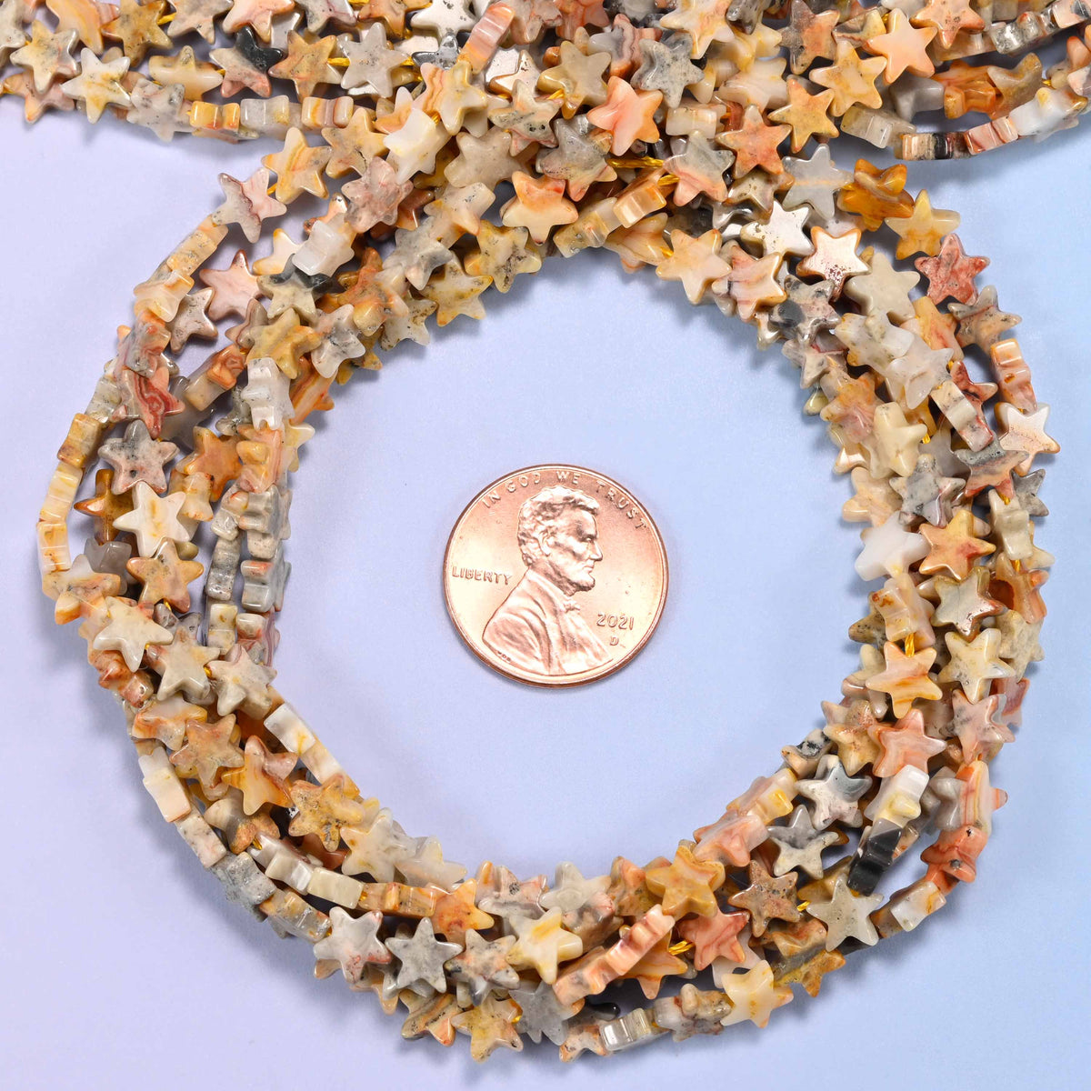 Crazy Agate flat star bead strands coiled around a US penny for size reference