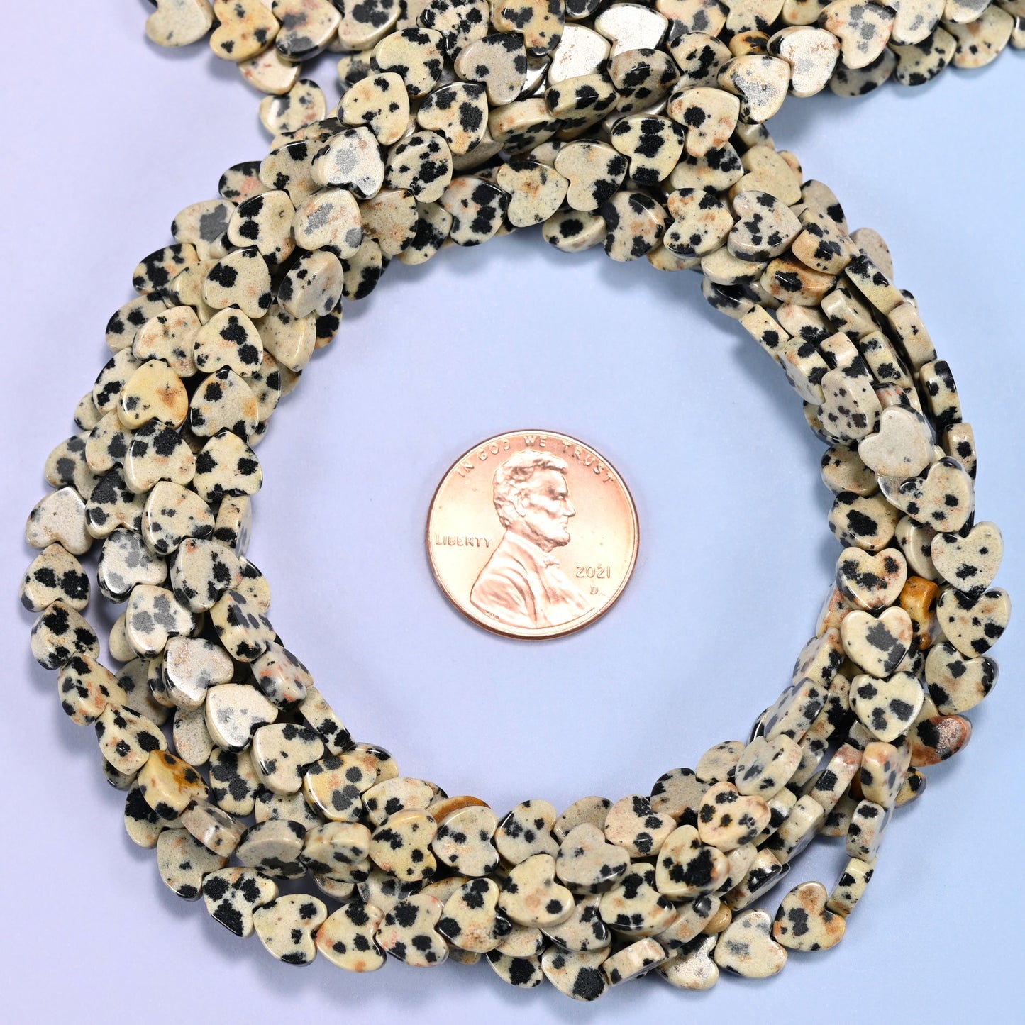 Dalmatian Jasper flat heart bead strands coiled around a US penny for size reference