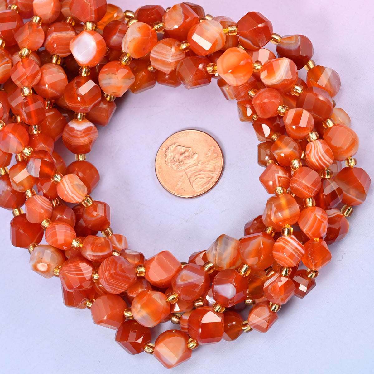 Dyed Red Stripe Agate faceted spiral twist bead strands coiled around a US penny for size reference