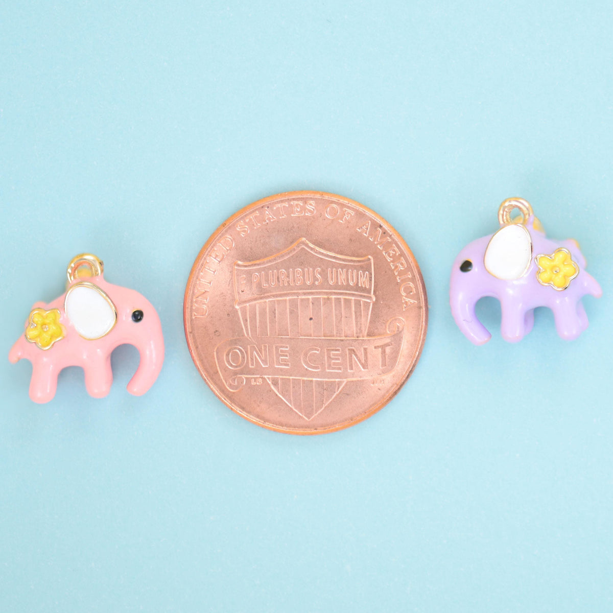 Pink and lilac enamel elephant charms shown either side of a US penny for size reference