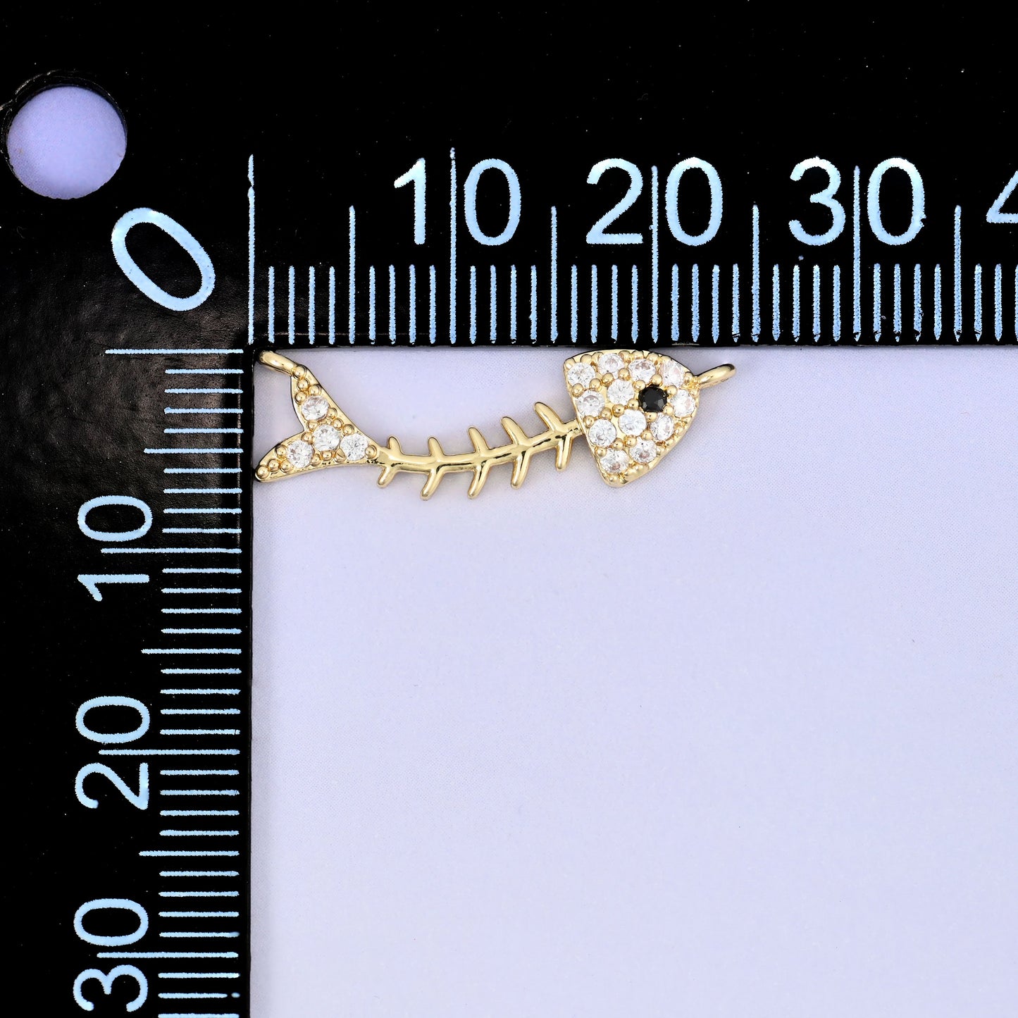 A fishbone zircon charm photographed beside a millimetre ruler for scale