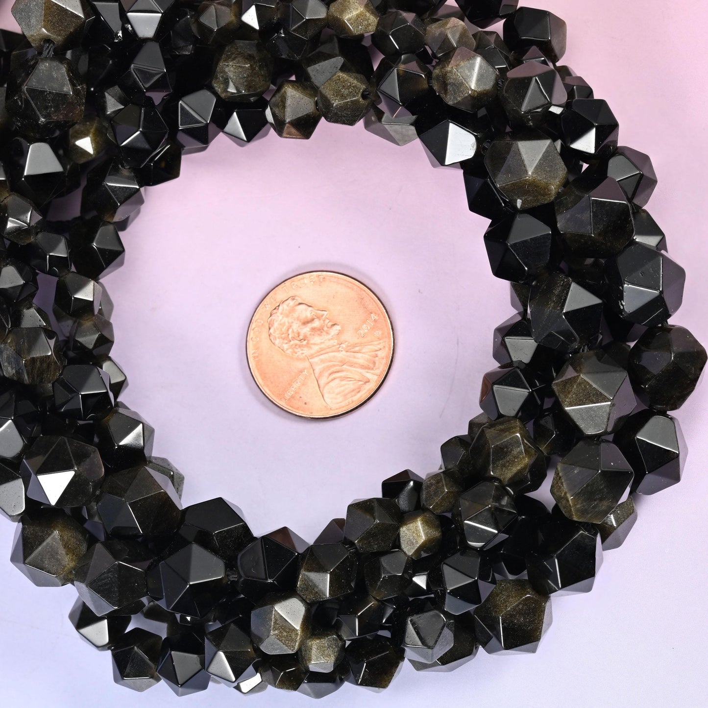Gold obsidian faceted diamond star cut bead strands coiled around a US penny for size reference