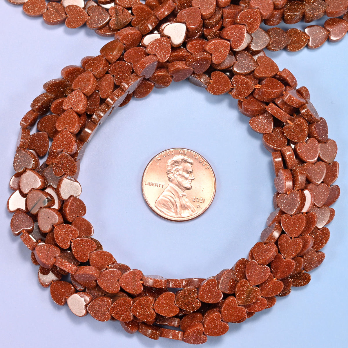 Gold Sandstone flat heart bead strands coiled around a US penny for size reference