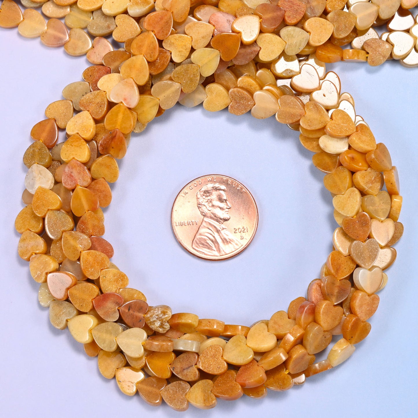 Gold Silk Jade flat heart bead strands coiled around a US penny for size reference