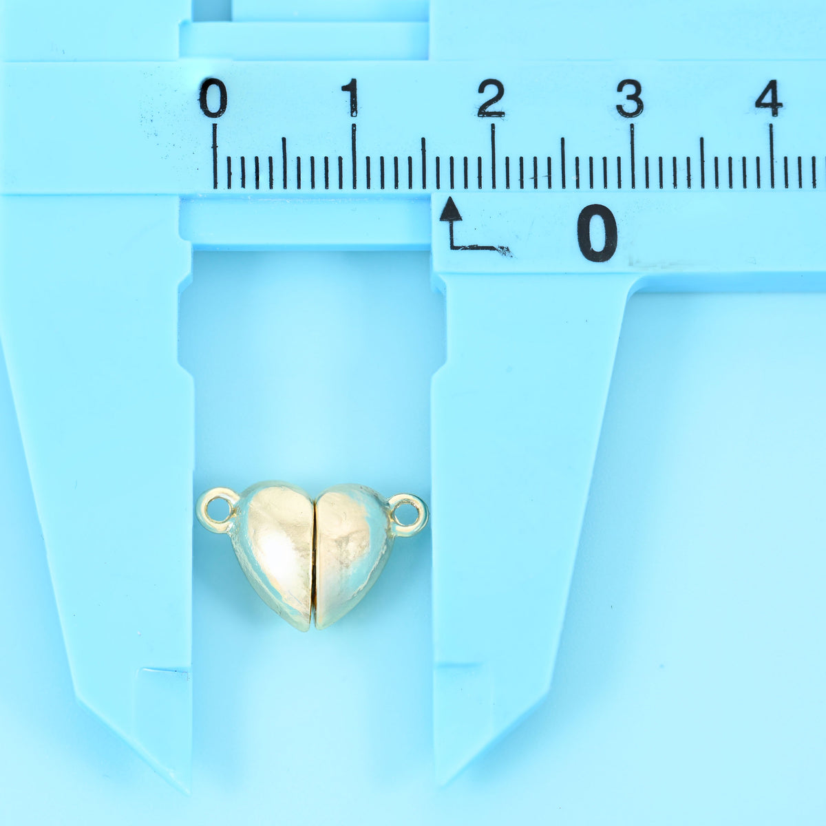 Gold heart magnetic clasp held in the jaws of a caliper for size reference