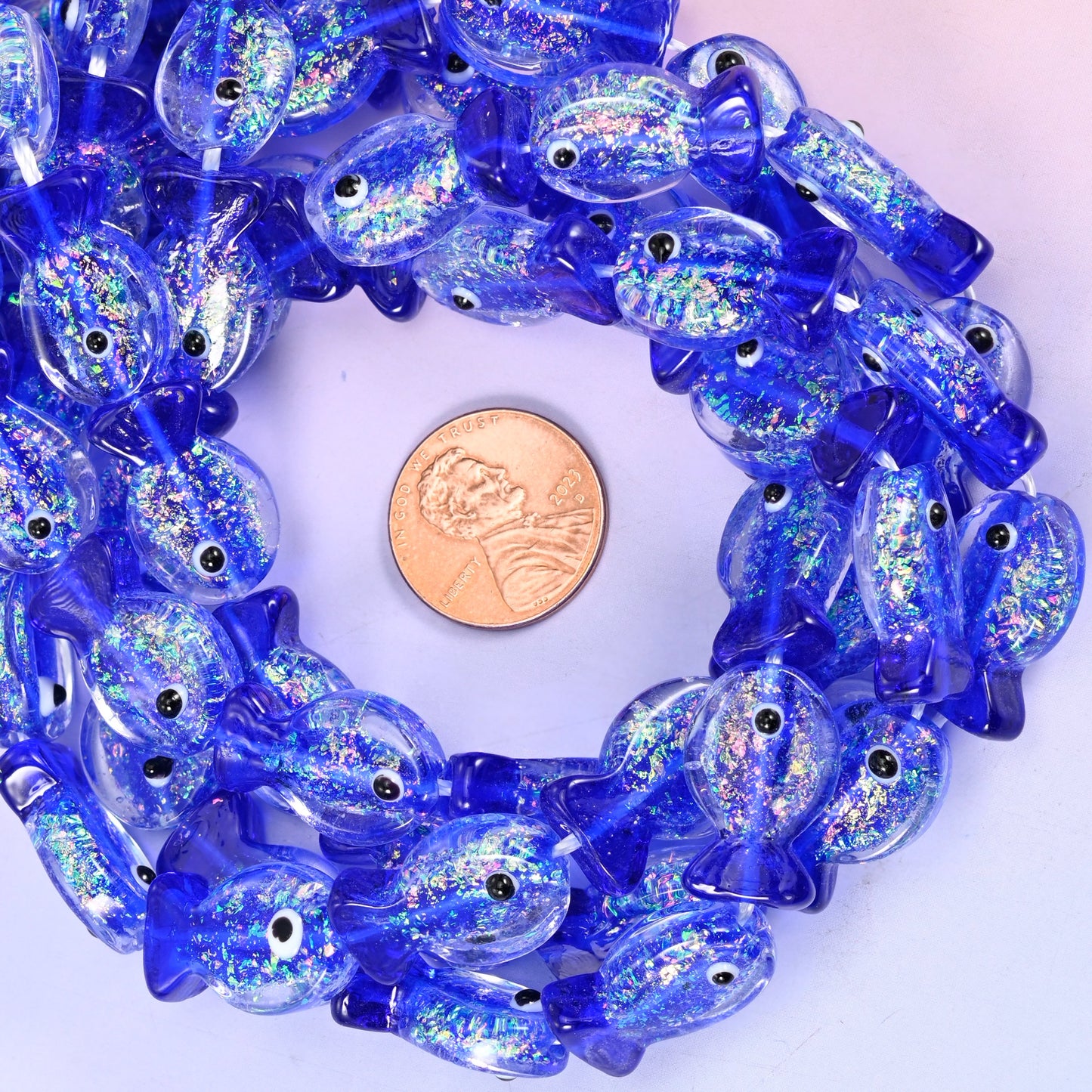 Iridescent Dark Blue Fish glass bead strands coiled around a US penny for size reference