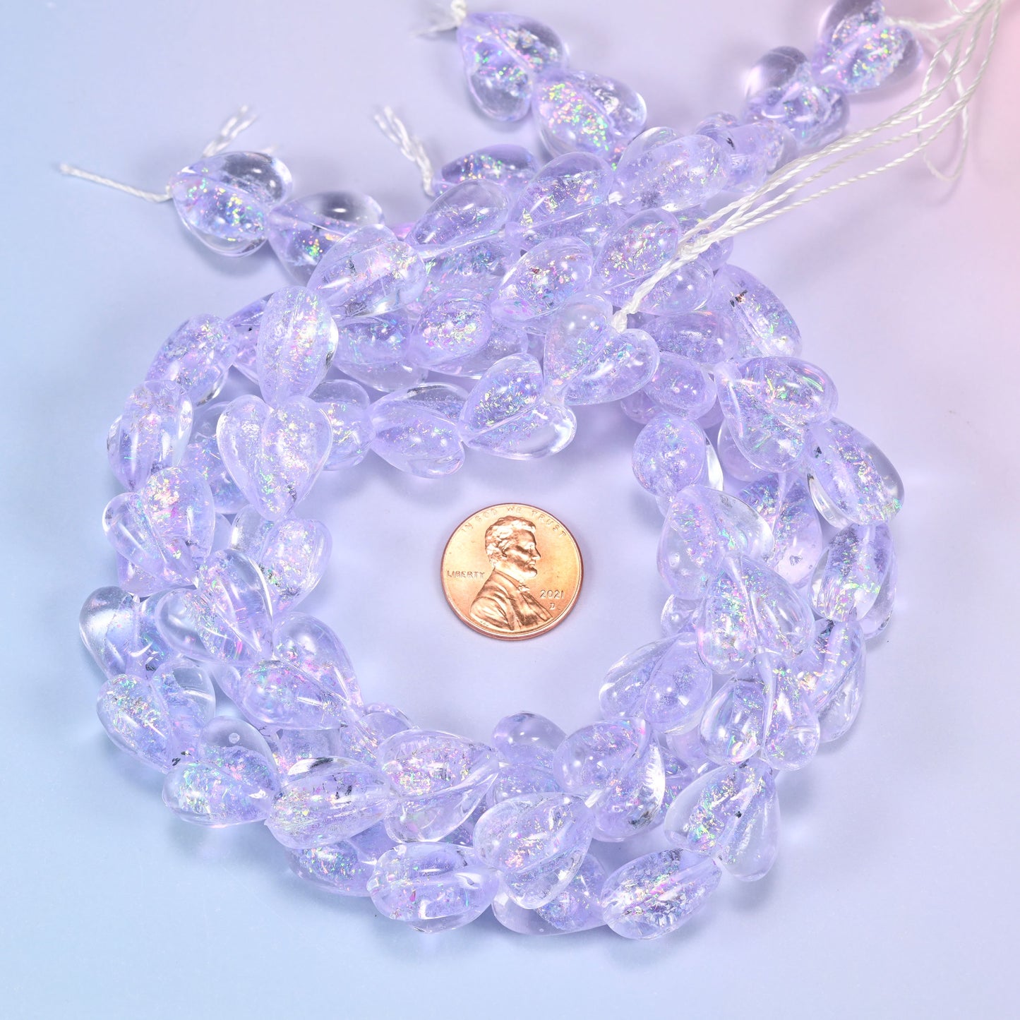 Iridescent Light Purple Heart glass bead strands coiled around a US penny for size reference