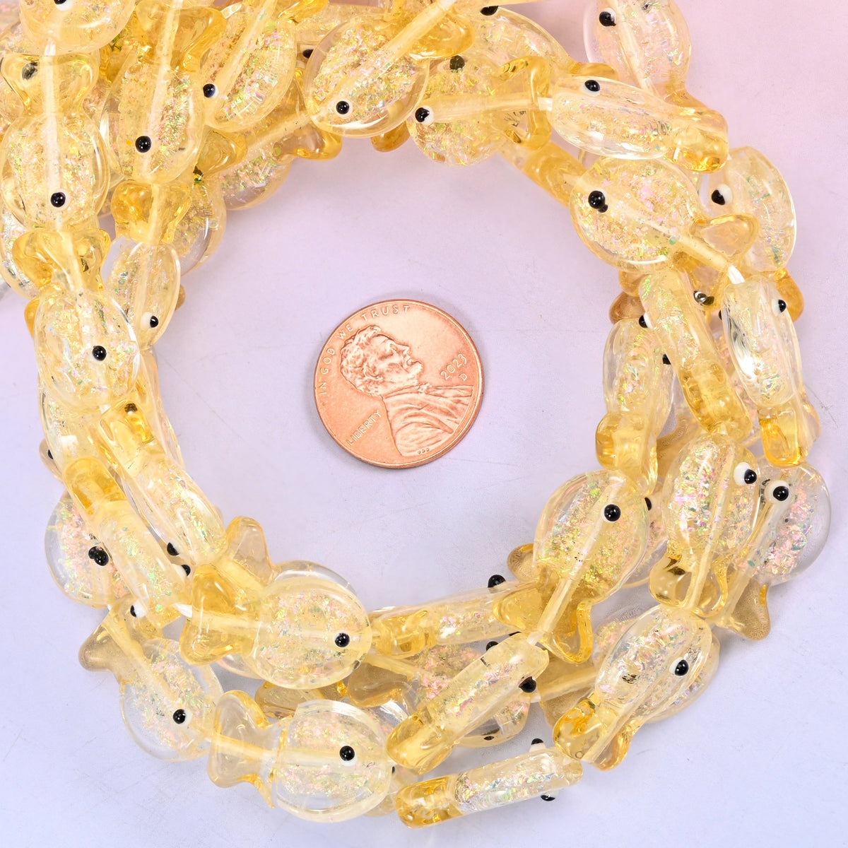 Iridescent Yellow Fish glass bead strands coiled around a US penny for size reference