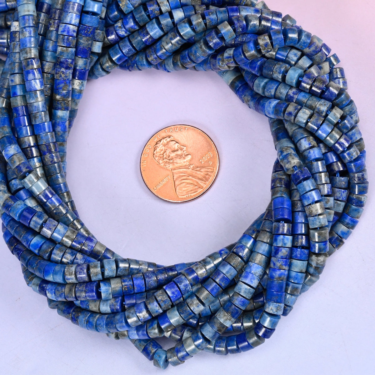 Lapis smooth heishi disc bead strands coiled around a US penny for size reference