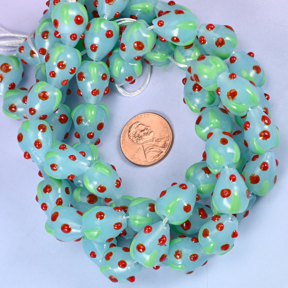 Light Blue Red Dots Strawberry glass bead strands coiled around a US penny for size reference