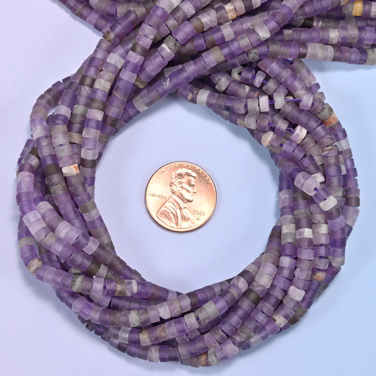 Matte Amethyst heishi disc bead strands coiled around a US penny for size reference