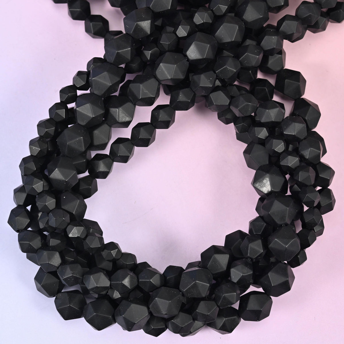 Matte black onyx faceted diamond star cut beads, strands coiled into a loop showing the flat black facets with no shine