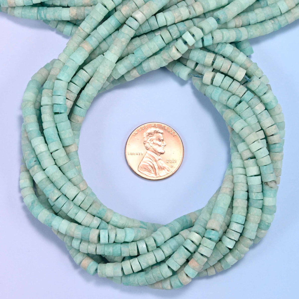 Matte Blue Amazonite heishi disc bead strands coiled around a US penny for size reference