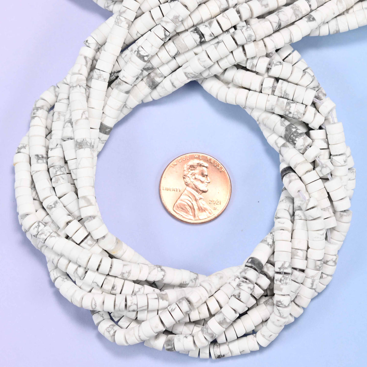 Matte White Howlite heishi disc bead strands coiled around a US penny for size reference