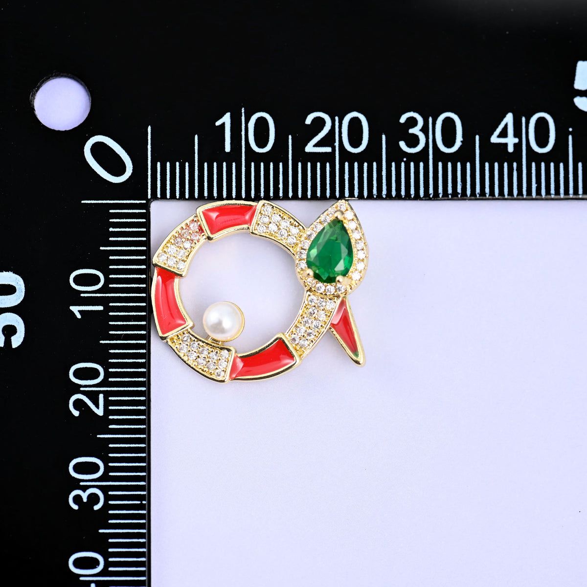 Round snake charm against a black millimetre ruler, the red enamel piece turned on its side with the green stone head pointing to the right.