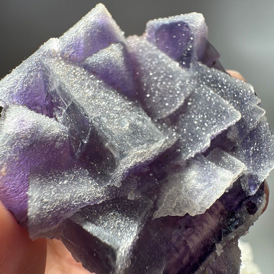 Close view of stepped fluorite cubes, sugary quartz crust breaking to show violet crystal beneath