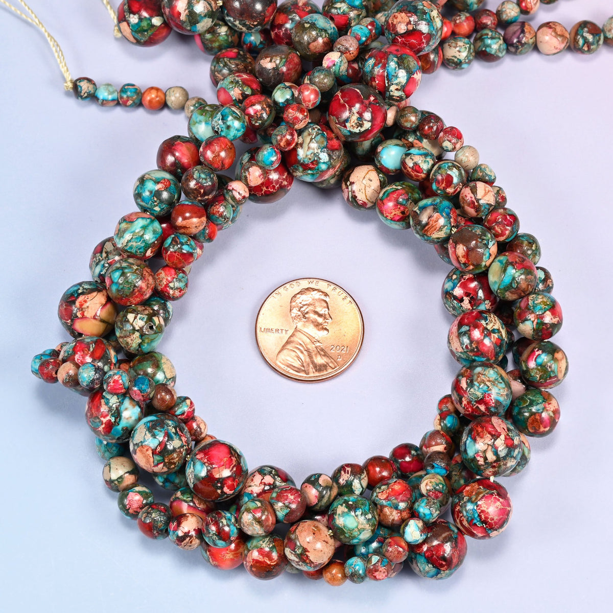 Red sea sediment jasper round beads coiled in loose rings with the knotted strand end at the top, shown with a US penny for scale.