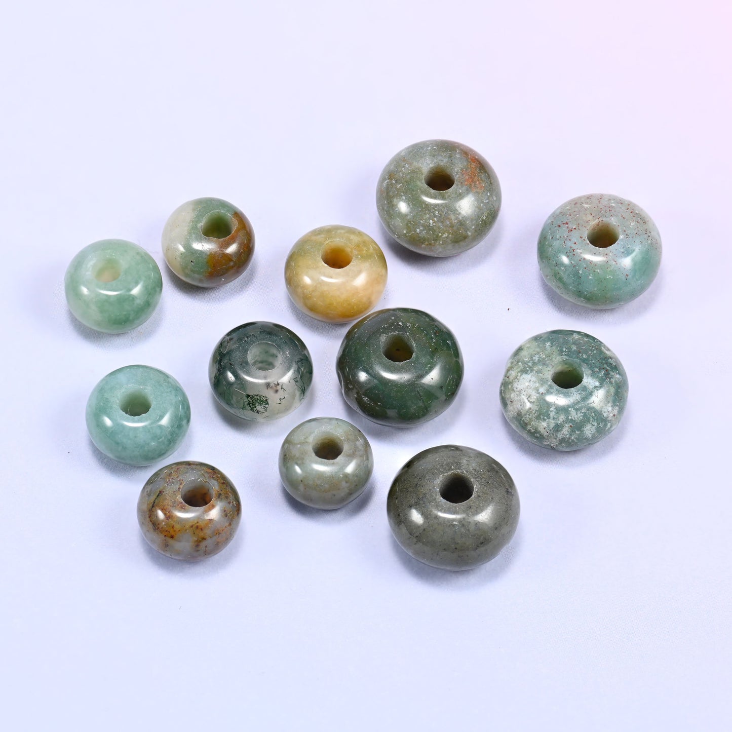 Close-up of individual loose Indian Agate beads laid out on a white surface, showing the large center-drilled hole and varied multicolor pattern of each bead.