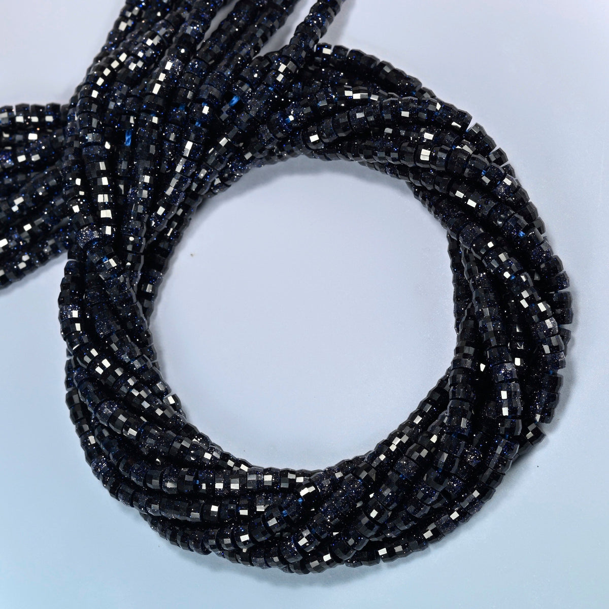 Blue sandstone faceted heishi disc beads coiled into overlapping loops, whole strands of sparkly dark blue glass