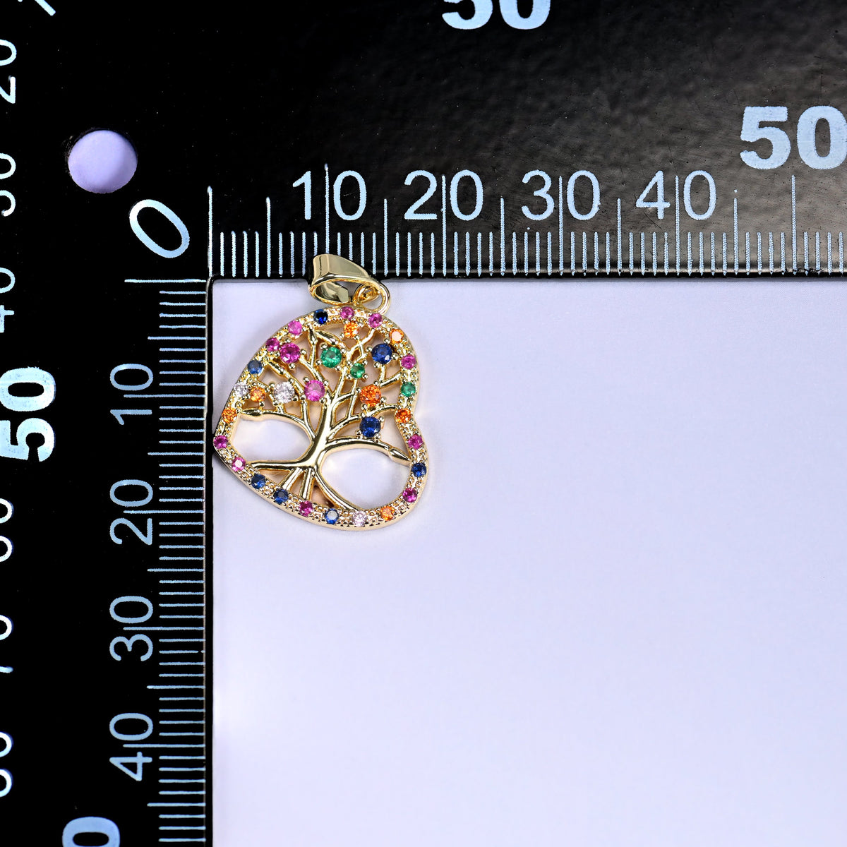 Gold heart tree of life zirconia charm on a black millimetre ruler, the heart measuring roughly 21mm across.