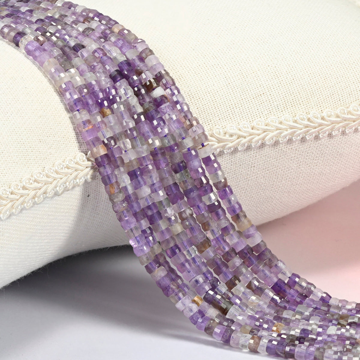 Amethyst faceted heishi disc beads 2x4mm, several strands draped over a white cushion