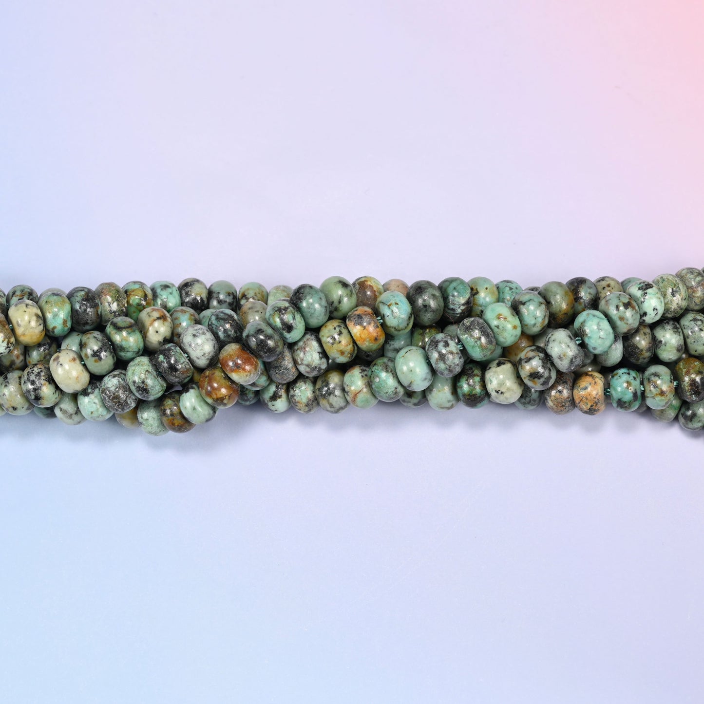 Bundled coil of African Howlite rondelle beads on a lavender background with a penny placed at the center for scale.