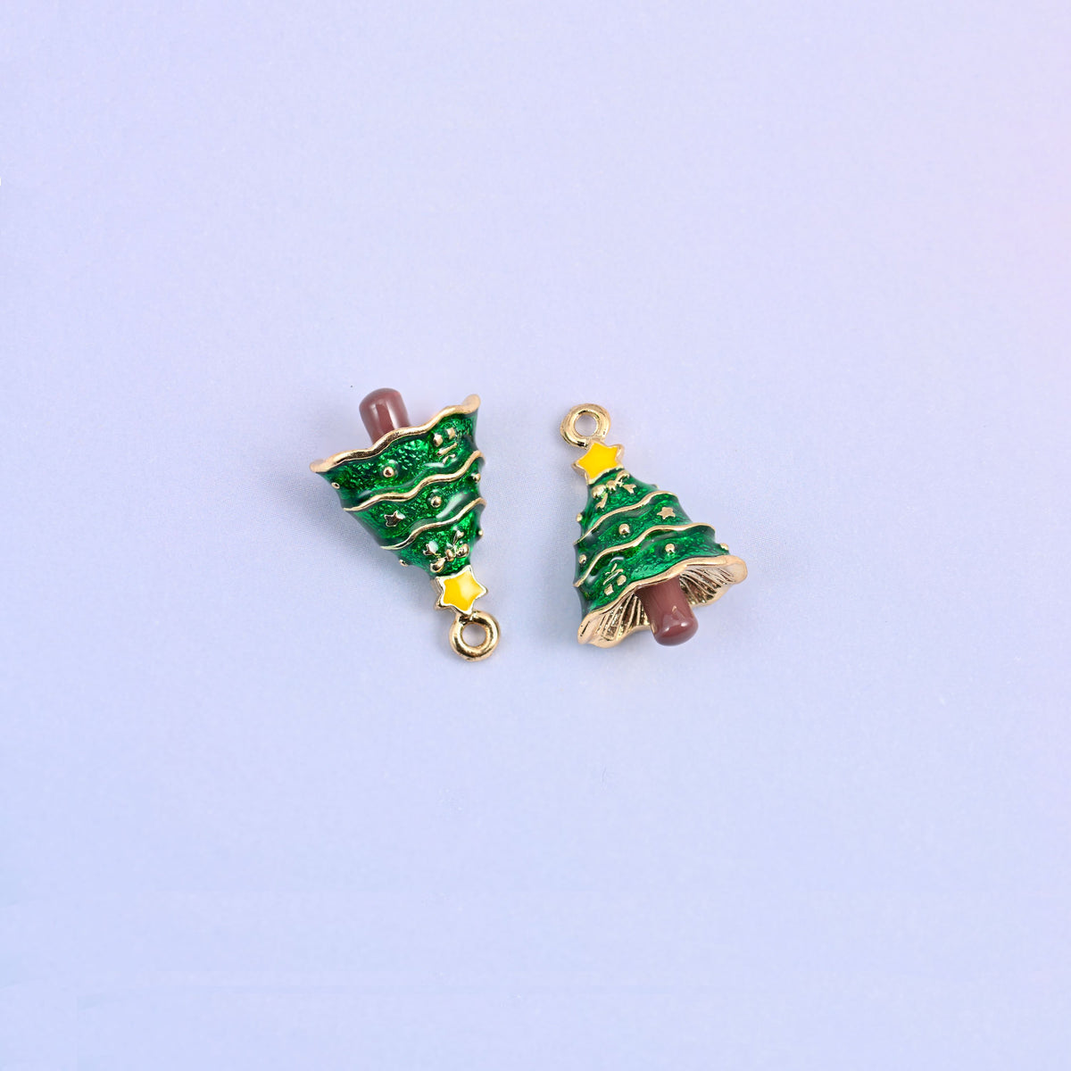 Two christmas tree charms tipped on their sides, showing the gold skirt and the brown enamel trunk.