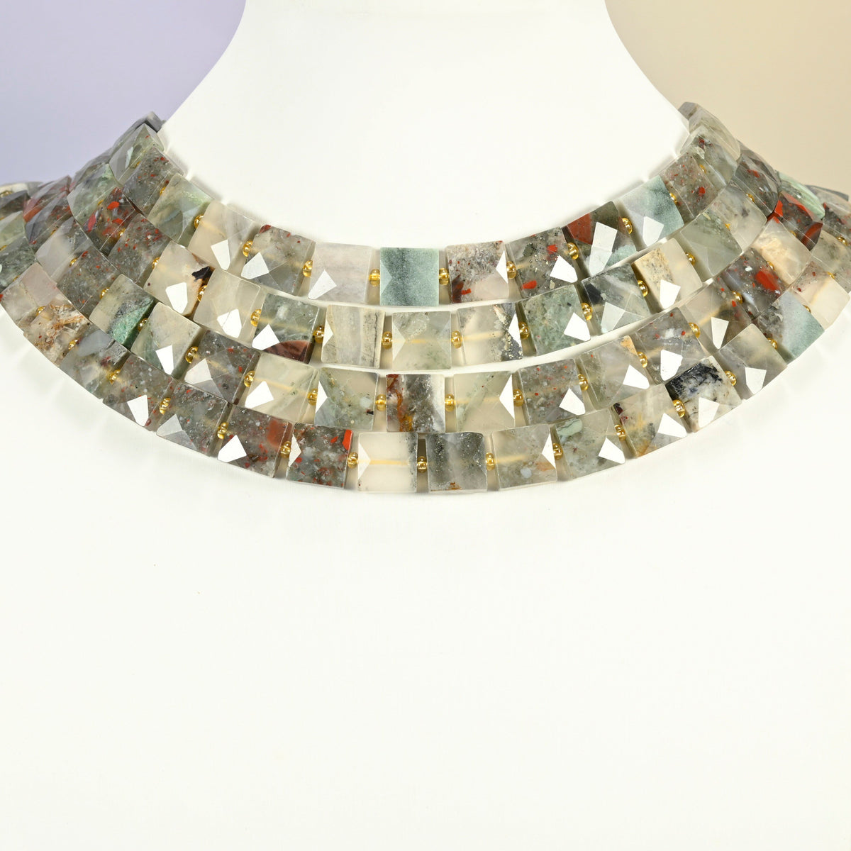 Natural African bloodstone faceted flat square strands arranged as a layered collar on a white display bust, gray-green beads across the neck