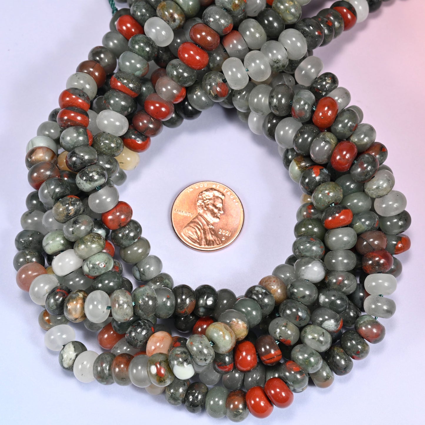 Multiple strands of African Bloodstone beads gathered together on a lavender surface, loose ends visible.