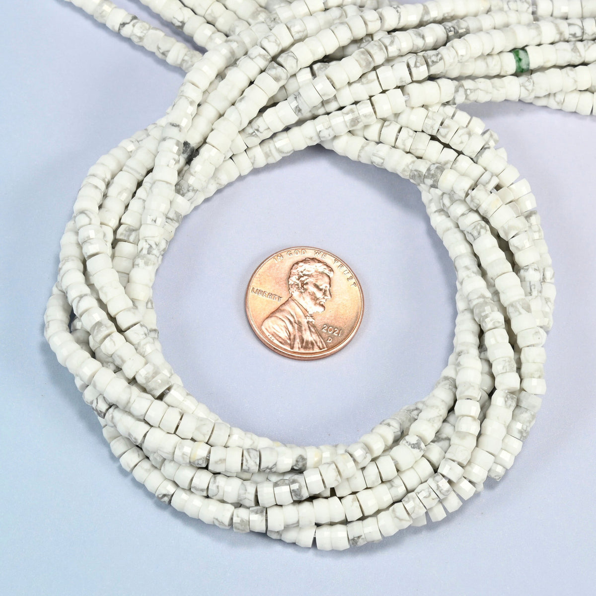 White howlite faceted heishi disc beads 2x4mm coiled in a loop around a US penny for scale, close-up of the faceted disc shape
