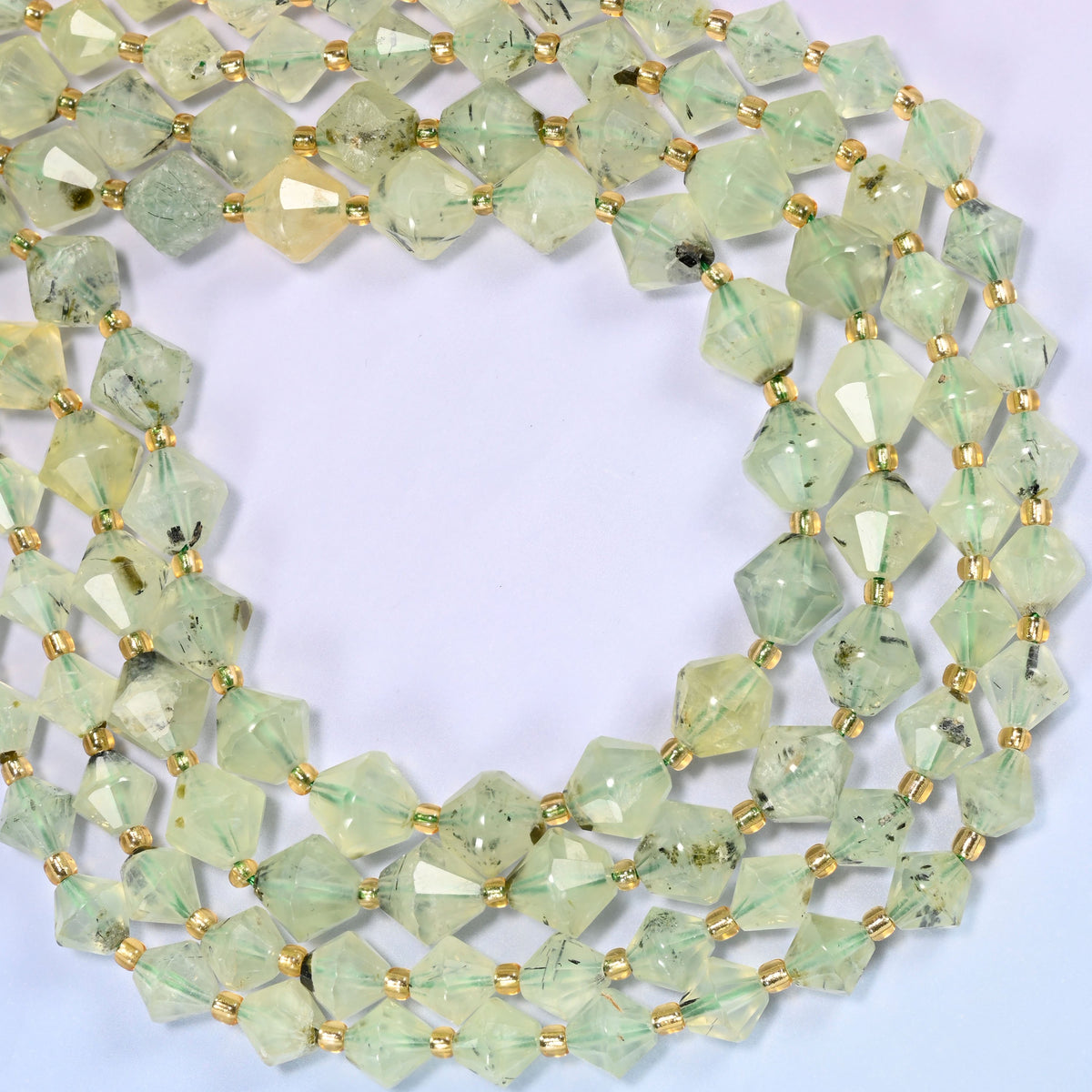 Green Prehnite faceted bicone beads, 8mm and 10mm, coiled into a loose circle on a light lavender background.