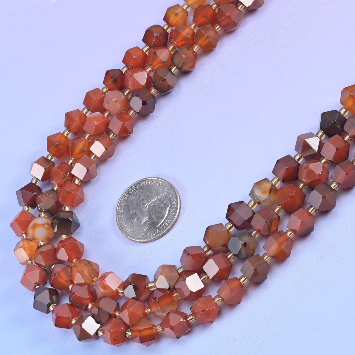 Faceted 8 sides diamond rhombus beads in dyed red strip agate curved around a US quarter laid flat for scale.