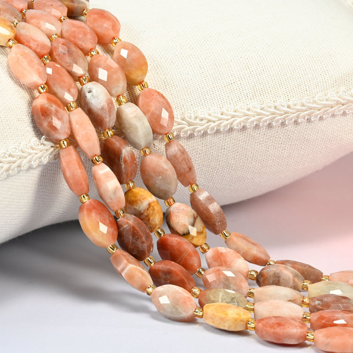 Red crazy agate faceted flat oval beads 9x14mm with small gold seed bead spacers, several strands draped over a white cushion