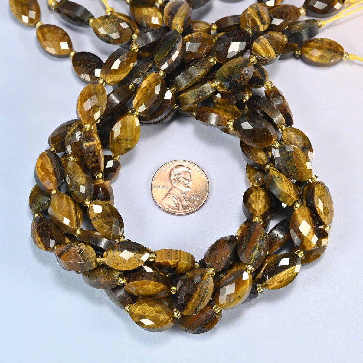 Tiger eye faceted flat oval beads 9x14mm coiled in a loop around a US penny for scale, close-up of the faceted flat oval shape