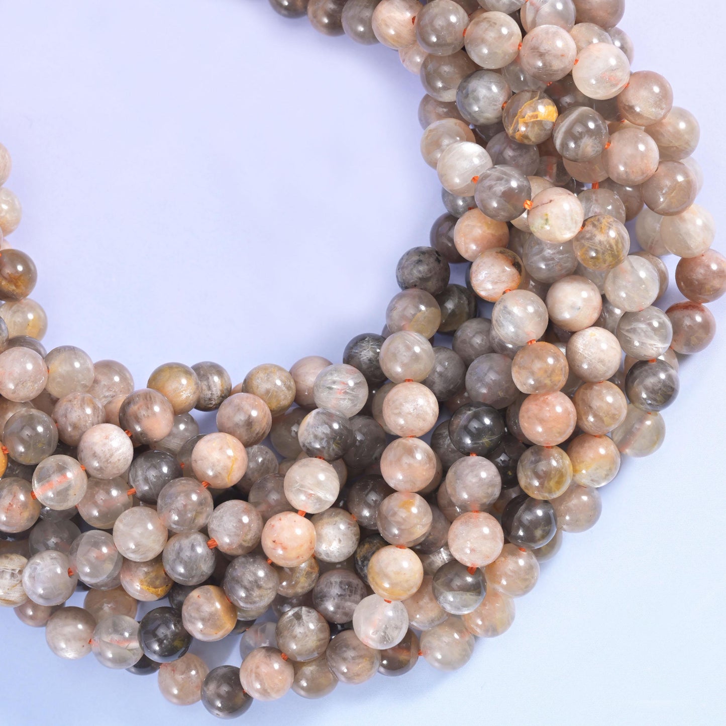 Warm grey, taupe and soft peach-beige rounds streaked with charcoal and cream, lit by the faint pearly sheen moonstone gives when the light rolls across it.