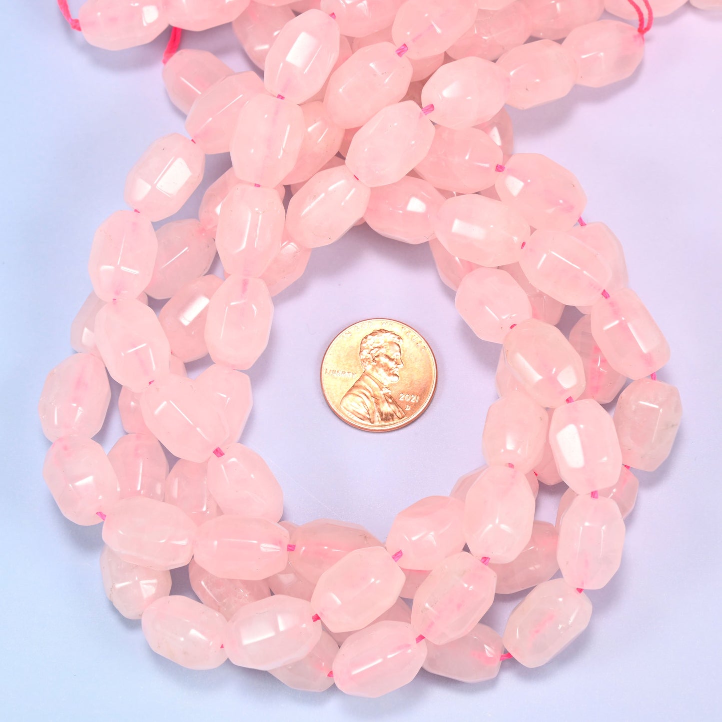 Close-up circular coil of Rose Quartz faceted barrel bead strands with a penny in the center for size comparison.