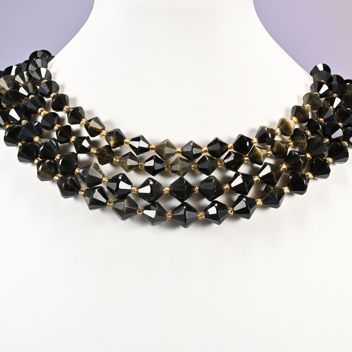 Gold obsidian bicone beads curved into a collar, the golden shimmer lifting on the beads that catch the light and disappearing on the rest.