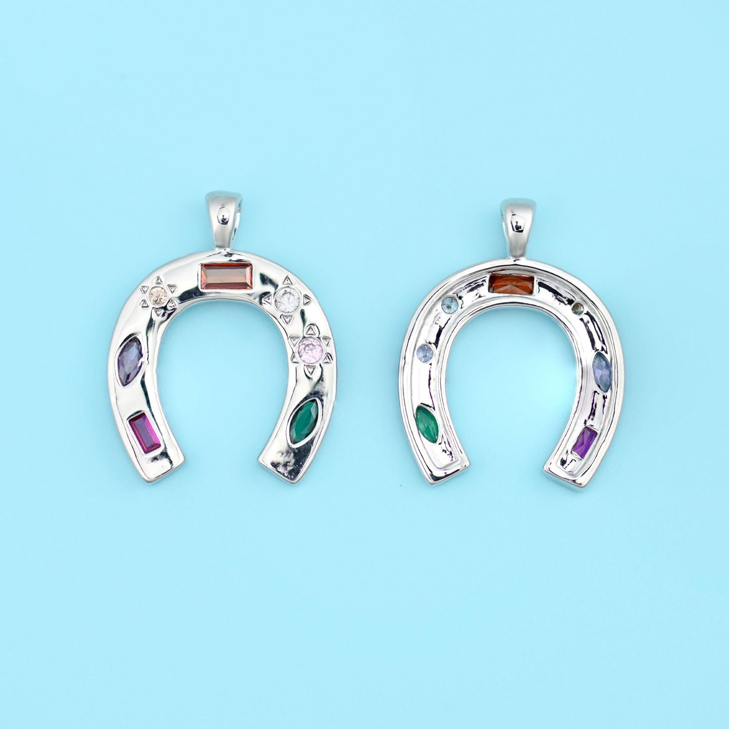 A horseshoe pendant set with coloured zircon stones in amber, deep purple, emerald green and rose, scattered between tiny…