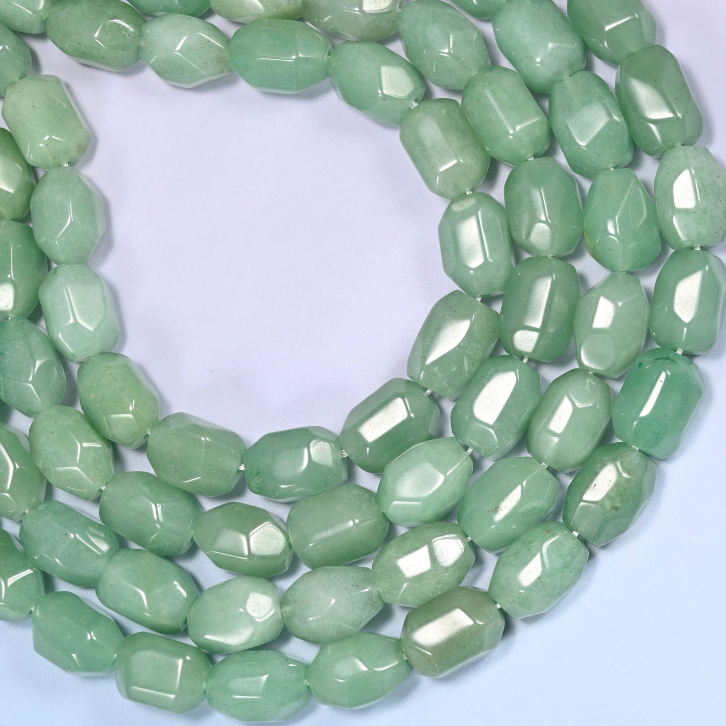 Circular coil of green faceted Aventurine barrel bead strands on a light lavender background with a penny in the center for size comparison.