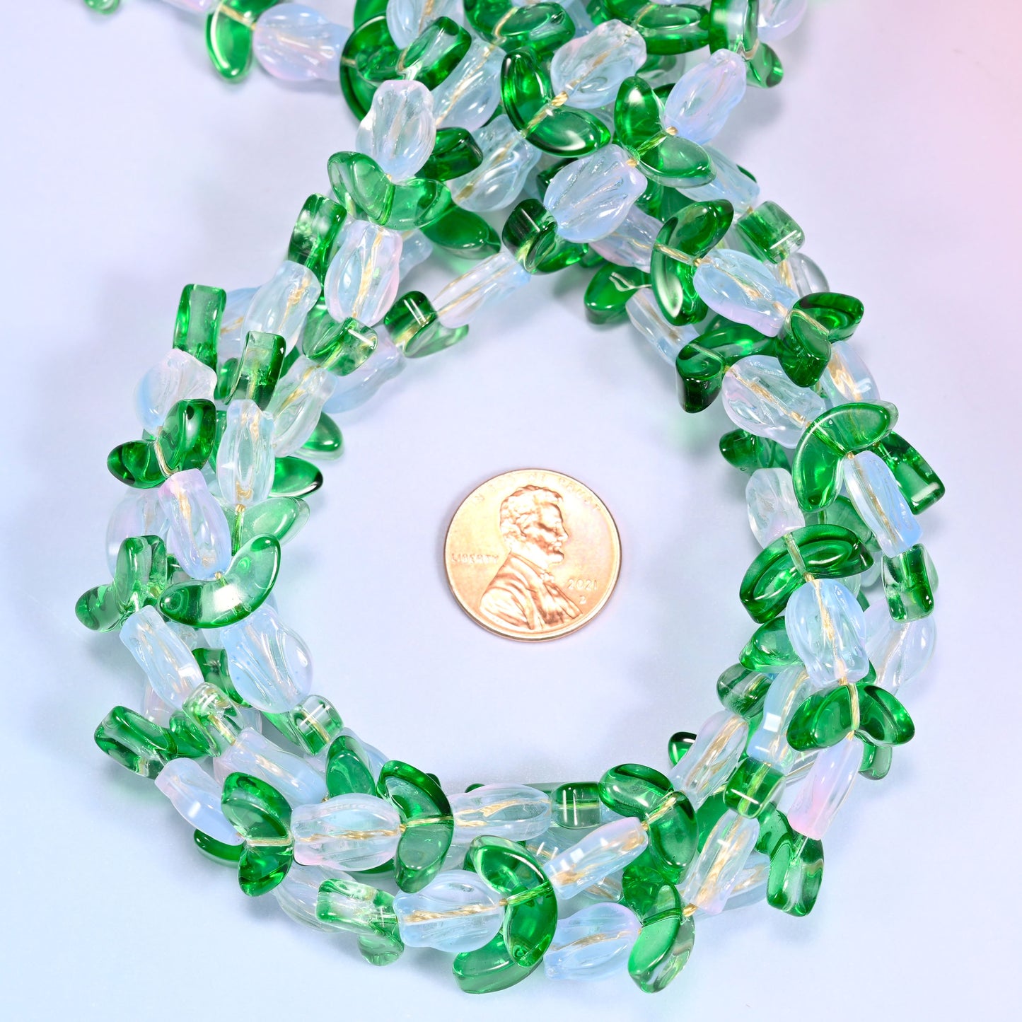 Horizontal row of white tulip and green leaf glass beads laid straight across a lavender background, showing the alternating pattern up close.