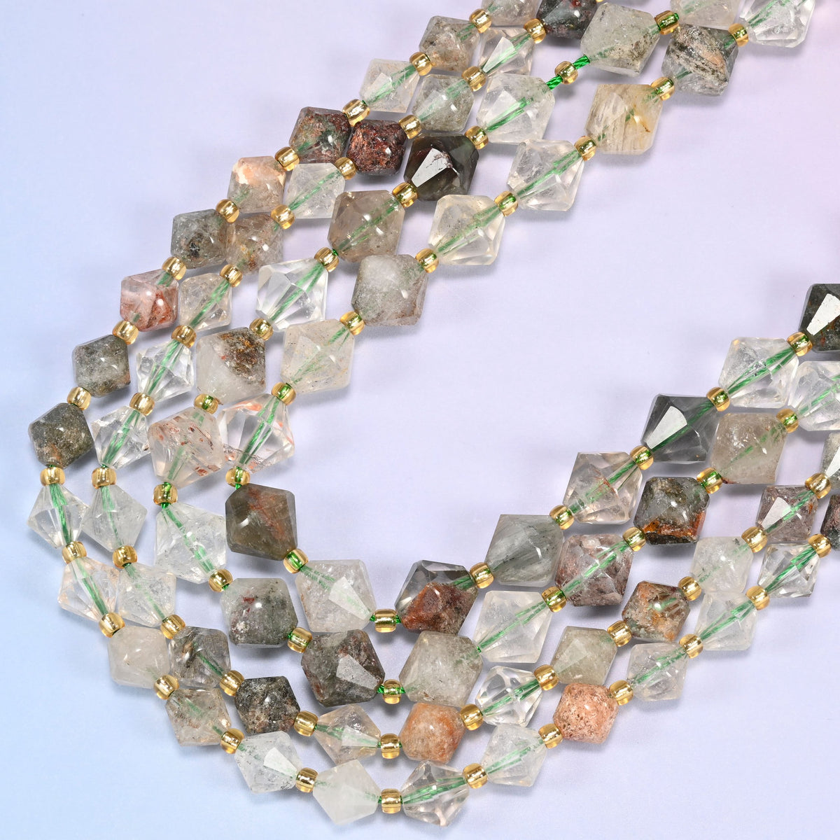 Green Phantom Quartz faceted bicone beads, 8mm and 10mm, arranged in a loose curved strand on a light lavender background.