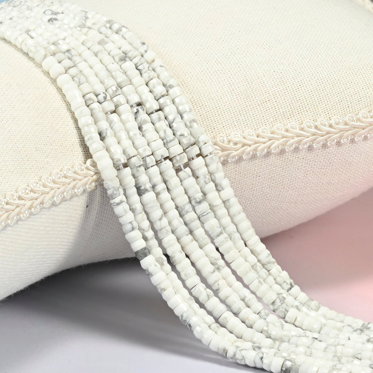 White howlite faceted heishi disc beads 2x4mm, several strands draped over a white cushion