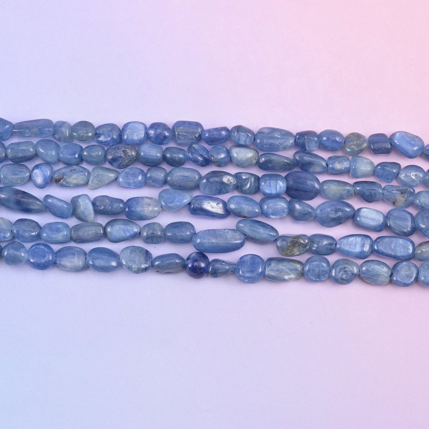Straight rows of 5-8mm kyanite nuggets laid flat, showing the range of pebble sizes on one strand