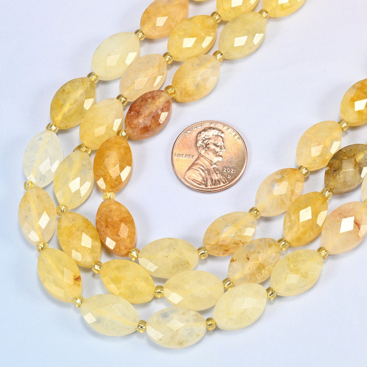 Close view of golden healer quartz faceted flat oval strands curving beside a US penny for scale