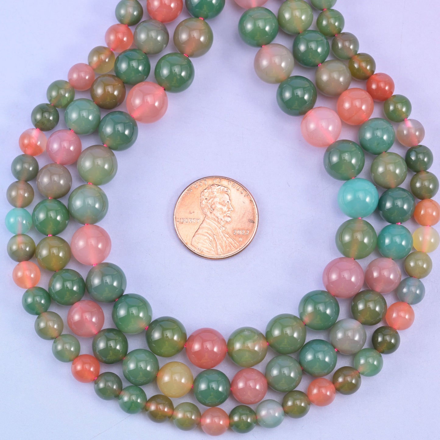 Green Yanyuan Agate smooth round beads coiled around a US penny for size reference, approximately 45 beads on a 14 inch strand at 8mm