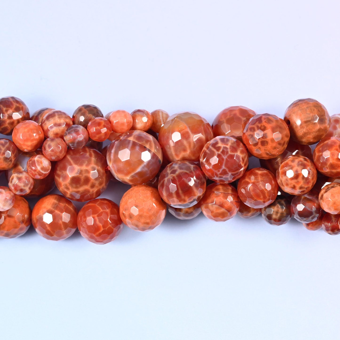 Hot coral-orange agate cut into crisp facets, with creamy white crackle patterning breaking across the surface