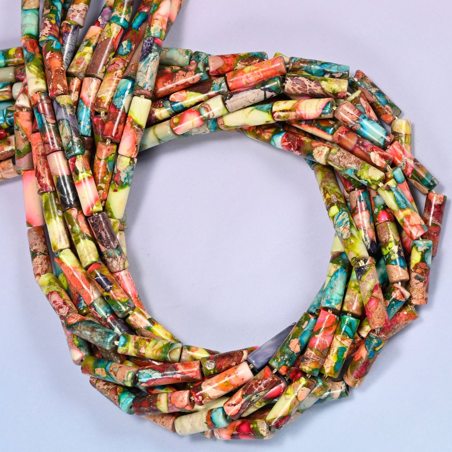Multiple strands of jasper tube beads gathered into a tight loop on a lavender surface, showing the dense pattern of turquoise, coral, and olive tones.