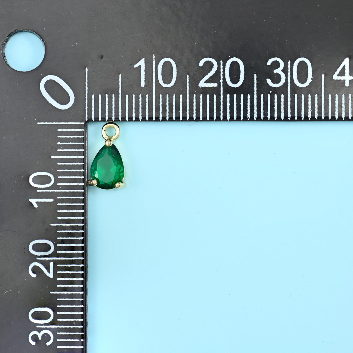 Teardrop zirconia charm in green on a black millimetre ruler, about 10mm long.