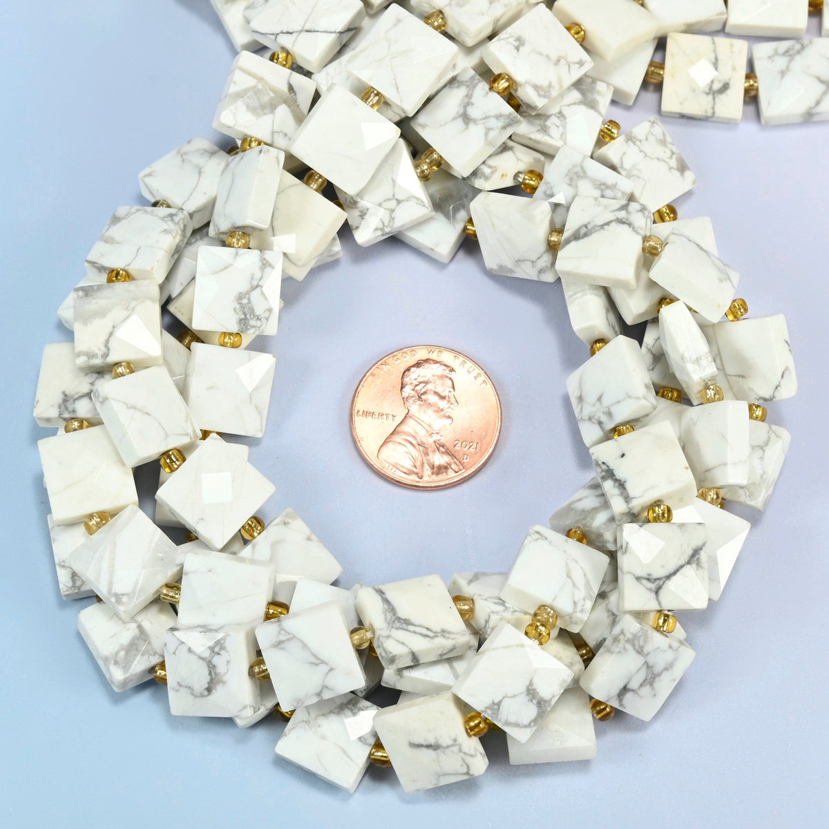White howlite faceted flat square beads 10x10mm coiled in a loop around a US penny for scale, close-up of the faceted flat square shape
